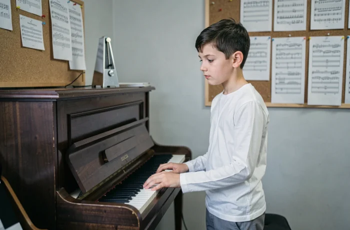 Préadolescent réfléchissant devant un piano droit dans une salle de répétition d'école de musique